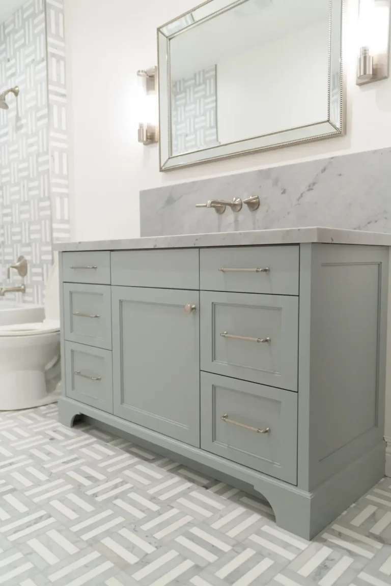 Light gray bathroom vanity with a marble countertop, wall-mounted faucet, rectangular mirror, and vertical storage.