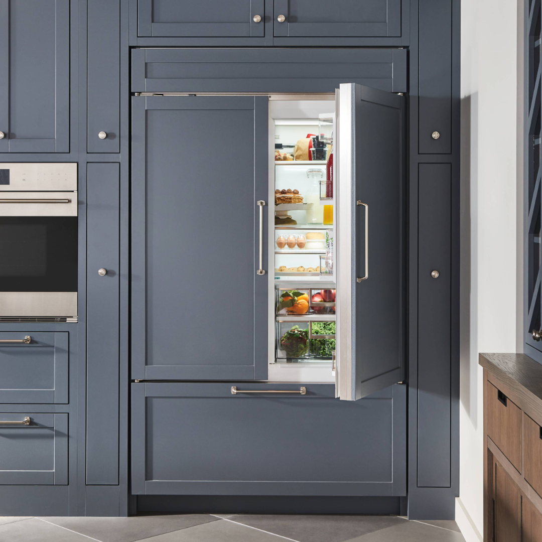 A built-in refrigerator with a partially open door reveals neatly organized food items inside a modern kitchen with gray cabinetry.