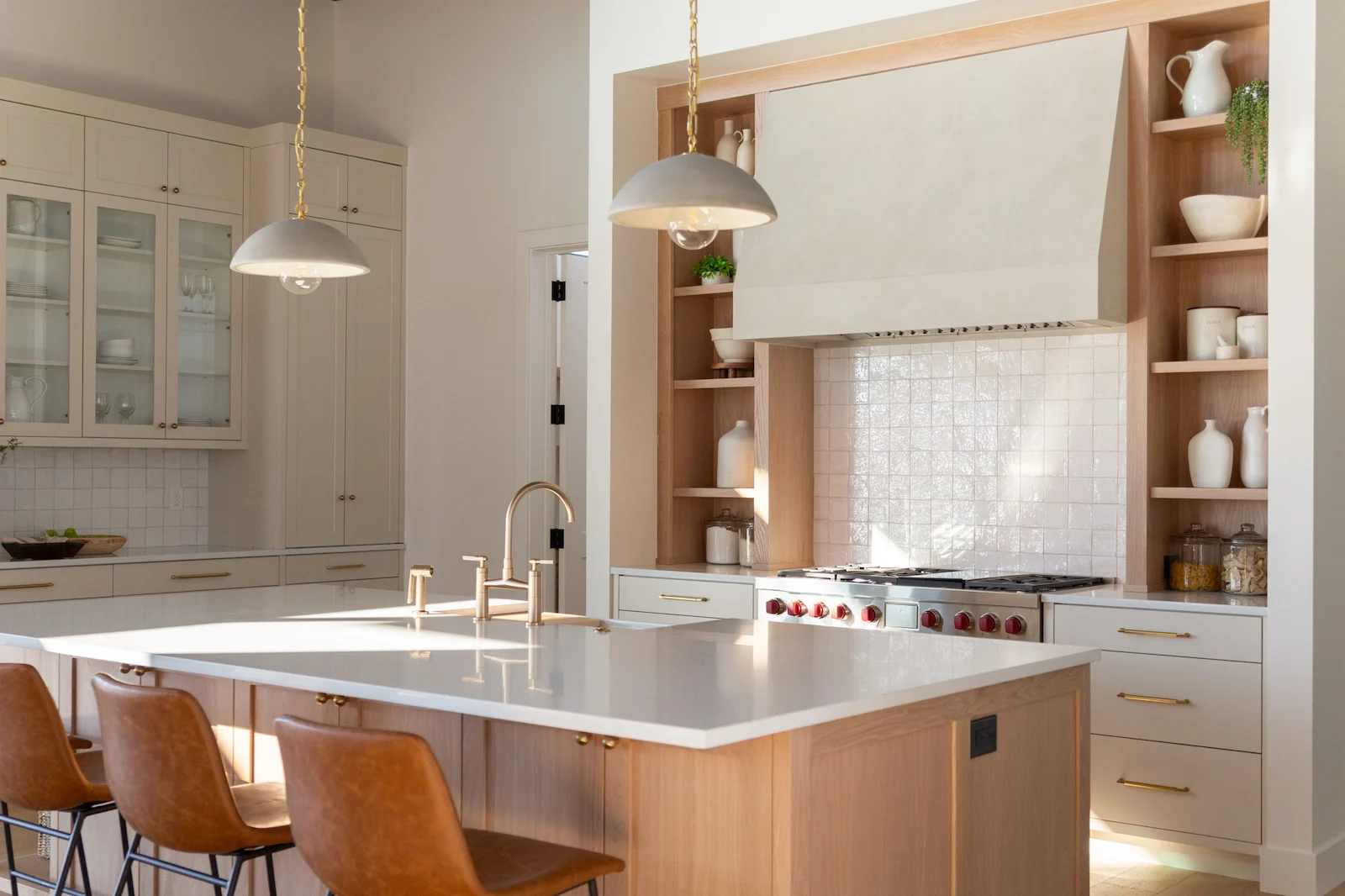 Modern kitchen with a large island, white countertops, brown leather bar stools, pendant lights, and open shelves around a tiled range hood.