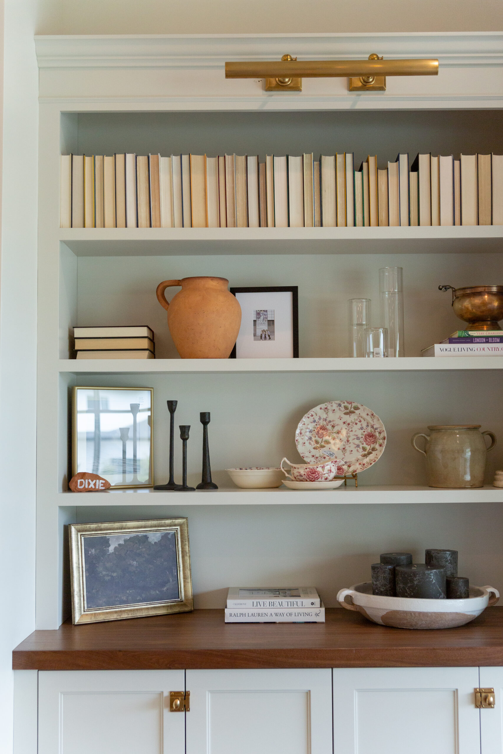A bookshelf featuring custom built-ins displays books, ceramics, candlesticks, framed photos, stacked plates, and decorative objects arranged neatly on crisp white shelves—a perfect example of elegant custom furniture design in Utah.