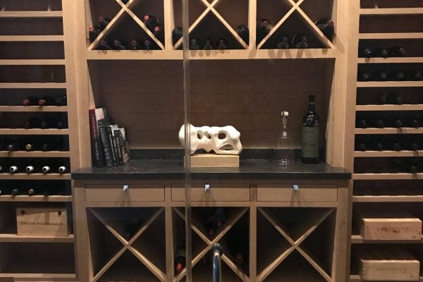 A wooden wine rack filled with wine bottles, books, a decorative item, a bottle of wine, and a wine glass on a black countertop creates an inviting focal point that complements modern kitchen cabinet colors and current kitchen cabinetry trends.